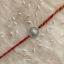 A Silver Wheel Of Progress Rakhi With Red Moli Thread For Bhaiya